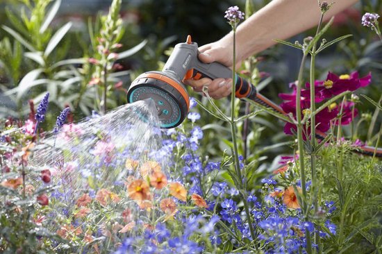 Grijze GARDENA spuit met oranje en blauwe accenten sproeit water in een bloembed.