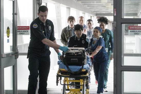 Ambulancepersoneel en ziekenhuispersoneel duwen een patiënt op een brancard naar binnen.