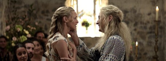 Amanda Seyfried en Meryl Streep kijken elkaar aan in een kerk. Streep raakt Seyfrieds gezicht aan. Beiden met lang, blond haar en zomerse kleding.