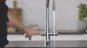 Vinger drukt op de knop van een chroomkraan waaruit kokend water stroomt.