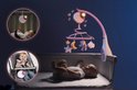 Baby in wieg en kinderstoel met roze muziekmobiel met maan, sterren en teddybeer.