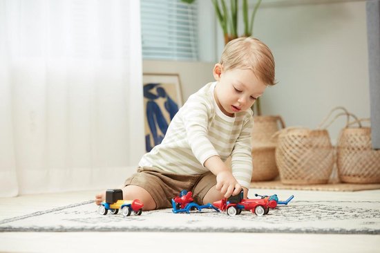Jongen speelt met een rood en blauw voertuig met wielen.