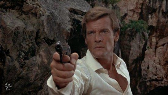Roger Moore als James Bond, gericht met een pistool, met een lichtgekleurde open overhemd, in een rotsachtige omgeving.