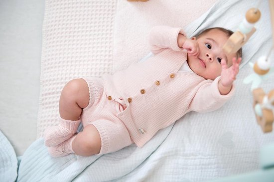 Baby in lichtroze gebreide set van Koeka. Set bestaat uit vestje, broekje en sokjes.
