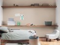 Kinderkamer met een bed, twee houten planken en een lichte fauteuil.