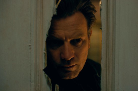 Close-up van Ewan McGregor die door een gat in een deur kijkt.
