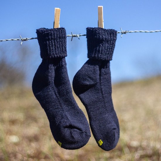 Twee donkerblauwe wollen sokken, gedroogd aan een waslijn, met kleine gele accenten aan de hiel.