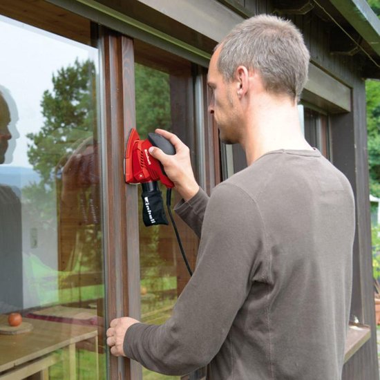 Man schuurt een houten kozijn met een rode Einhell schuurmachine met stofzak.