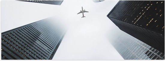 WallClassics - Poster Glanzend – Vliegtuig vliegend tussen Gebouwen - 90x30 cm Foto op Posterpapier met Glanzende Afwerking