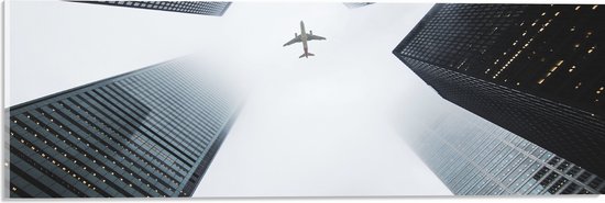 WallClassics - Acrylglas - Vliegtuig vliegend tussen Gebouwen - 60x20 cm Foto op Acrylglas (Met Ophangsysteem)