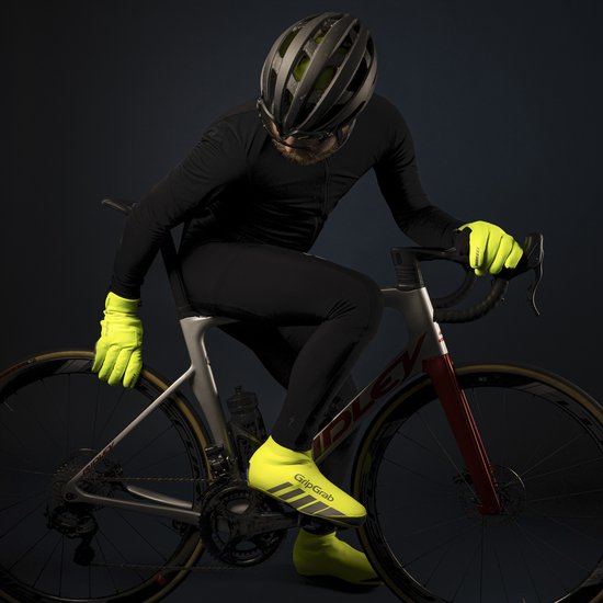 Een man op een racefiets draagt een zwarte outfit en gele handschoenen en overschoenen.