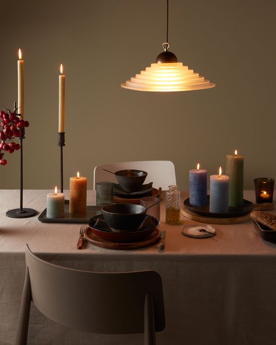 Een gedekte tafel met verschillende brandende stompkaarsen, borden en een hanglamp.