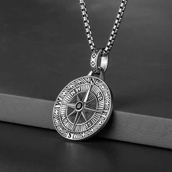 Zilverkleurige ketting met kompasroos hanger op donkere, getextureerde achtergrond.