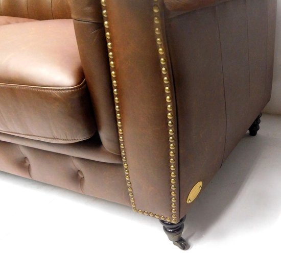 Detail van een bruine Chesterfield bank van leer, met klinknagels.