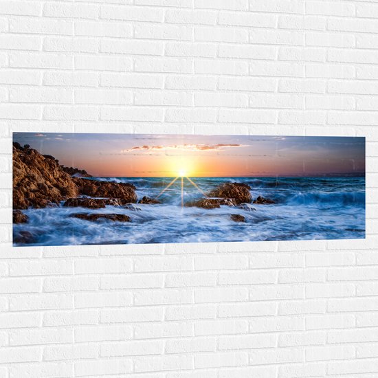 WallClassics - Muursticker - Felkleurige Zonsondergang achter Wilde Zee - 150x50 cm Foto op Muursticker