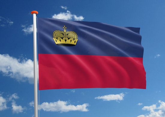 De vlag van Liechtenstein wappert tegen een blauwe hemel met witte wolken. De vlag is blauw en rood met een gouden kroon.