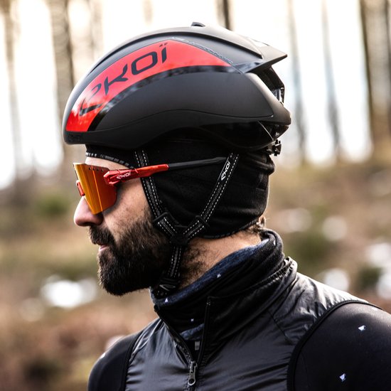 Profiel van een man met baard, die een zwarte fietsmuts, helm en oranje bril draagt.
