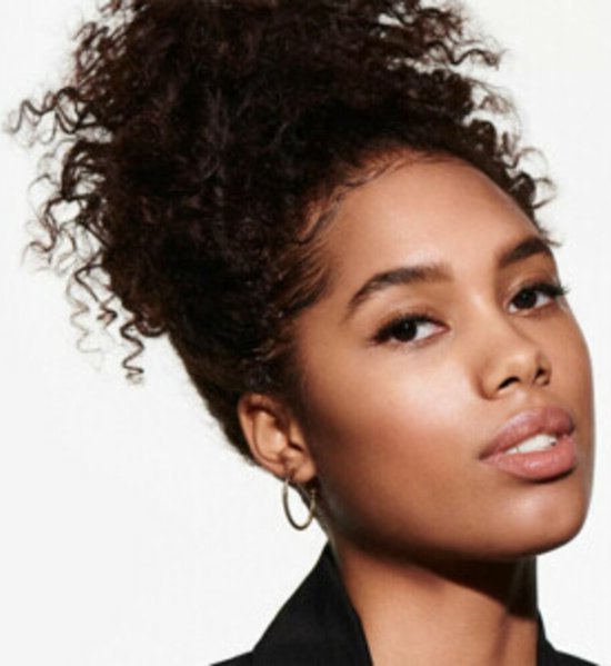 Model met bruin krullend haar opgestoken in een knot, met zwarte blazer.