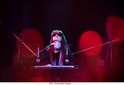Een vrouw met lang haar en zonnebril speelt keyboard in een verlichte studio met rode lichten.