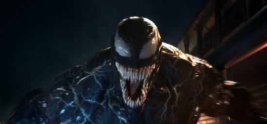 Close-up van het zwarte, grote wezen Venom met grote tanden en witte ogen, kijkend naar de camera.