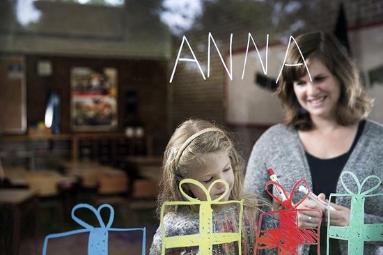 Vrouw en meisje tekenen cadeautjes en de naam 'Anna' op een raam.