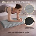 Grijze trainingsmat met bergmotief, met detail van de antislipstructuur. Vrouw doet een plankoefening.
