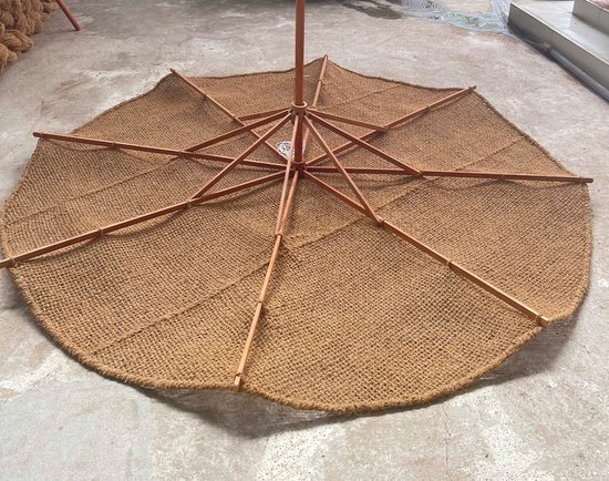 Open bruine kokos parasol liggend op de grond, van onderaf bekeken met het houten frame.