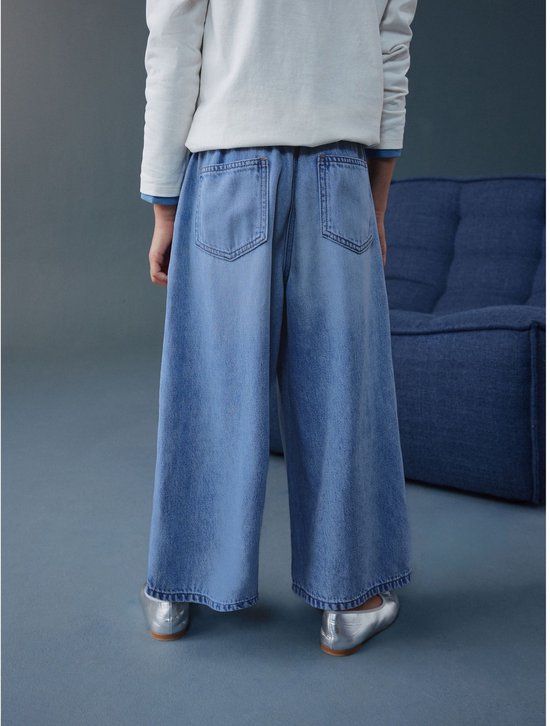 Kind draagt wijde, ronde jeans in lichtblauw denim, van achteren gezien.