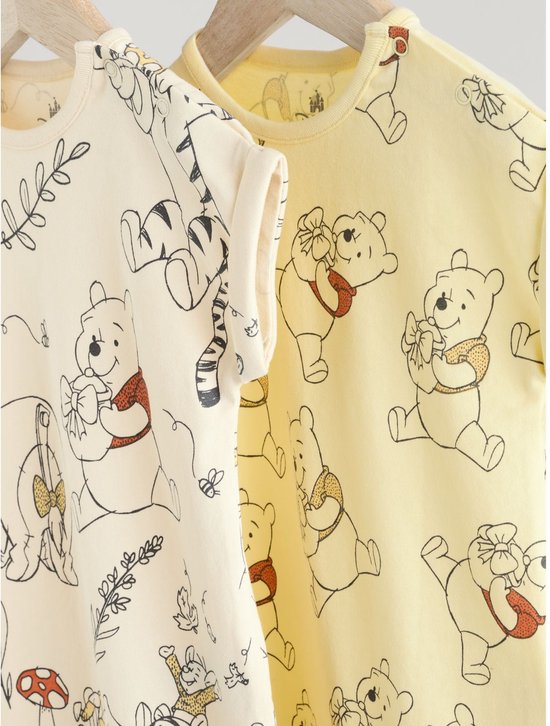 Twee rompertjes met opdruk van Winnie de Poeh, een crèmekleurige met Eeyore en Tigger, een gele met Winnie de Poeh.