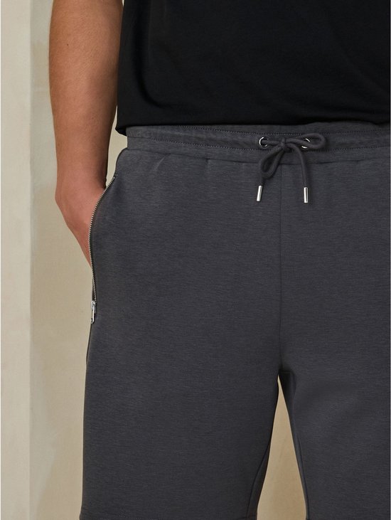 Close-up van de tailleband van een grijze jersey short met trekkoord en metalen uiteinden.