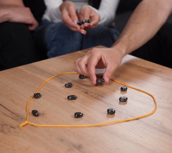 Een hand plaatst een magneet op een gele lijn op een houten tafel.