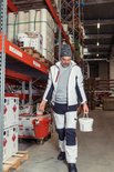Man met grijze jas en werkbroek met witte, grijze en zwarte panelen, draagt emmers.