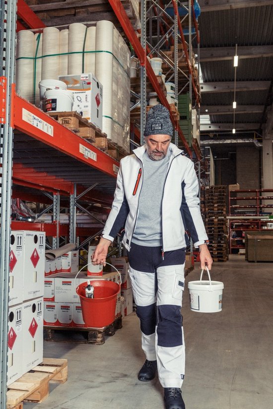 Man met grijze jas en werkbroek met witte, grijze en zwarte panelen, draagt emmers.