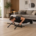 Man in een woonkamer doet een push-up met een zwarte optrekstang op de vloer.