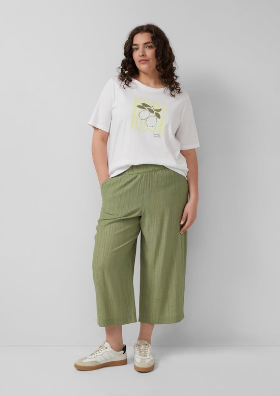 Model draagt olijfgroene culotte met crinkle stof, wit T-shirt met citroenprint en sneakers.