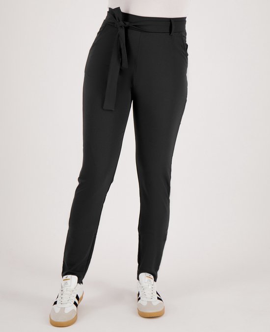 Een vrouw in een zwarte broek met hoge taille, strikceintuur en witte sneakers met strepen.