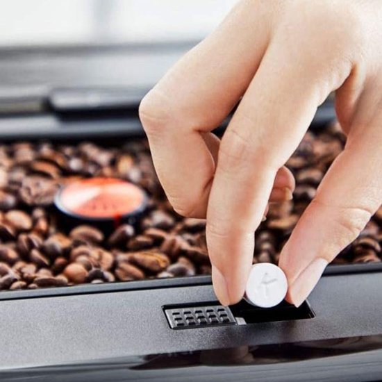 Hand plaatst een witte Krups reinigingstablet in een koffiemachine, tussen de koffiebonen.
