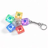 Vier transparante toetsenbord-fidget-keychains met gekleurde kapjes (rood, blauw, groen, geel) en lichtjes, met een zilveren sleutelring.