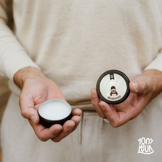 Handen houden een potje met 'WAX VOOR HAAR EN BAARD' van 100% LEUK, deksel ernaast.