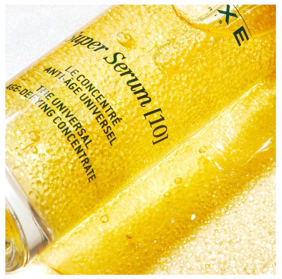 Gouden serum met gele parels en bubbels, met tekst 'Super Serum [10] LE CONCENTRÉ ANTI-ÂGE UNIVERSEL'.