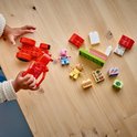 Kinderhanden bouwen met LEGO Duplo Peppa Pig tractor, marktkraam, poppetjes en bouwstenen op een houten tafel.