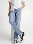 Jongen leunt op een blok in een lichtblauwe spijkerbroek met een witte T-shirt en zwart-witte sneakers.
