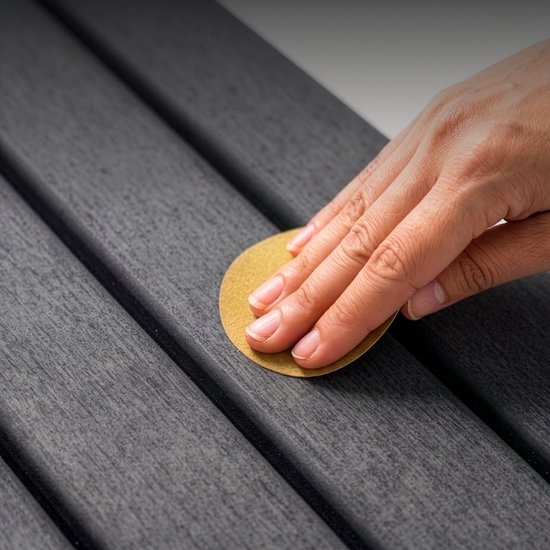 Een hand schuurt zachtjes over de geribbelde textuur van een donkergrijze badmat.