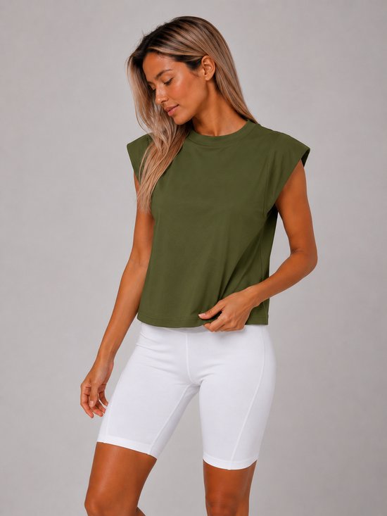 Vrouw met een groene, mouwloze crop top en witte fietsbroek, die aan de voorkant staat.