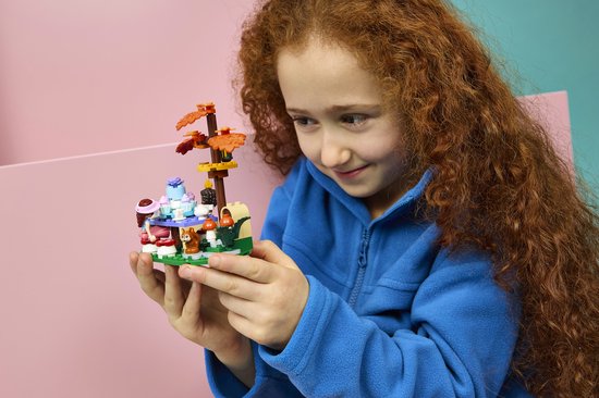 Meisje met krullend rood haar houdt LEGO Friends bosfeest speelset vast, met eekhoorn en cupcakes.
