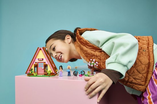 Kind kijkt naar een Lego Friends speelgoedhuisje met roze accenten en poppetjes op een roze tafel.