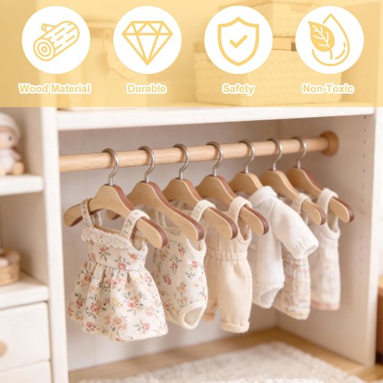 Houten kleerhangers met kinderkleding, waaronder een bloemenjurk, rompertjes en jasjes. Iconen voor hout, duurzaamheid, veiligheid en niet-giftig.