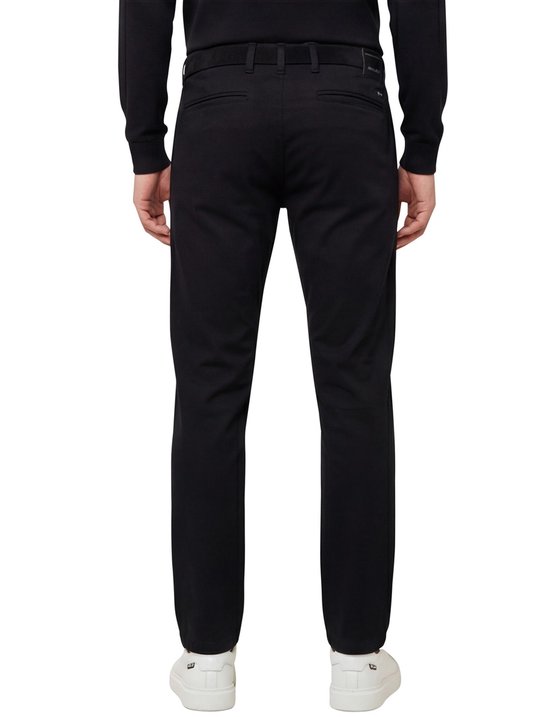 Achterkant van man met zwarte chino broek en witte sneakers.