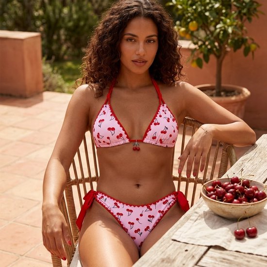 Model in een roze bikinitop en bikinbroek met kersenprint en rode randen.
