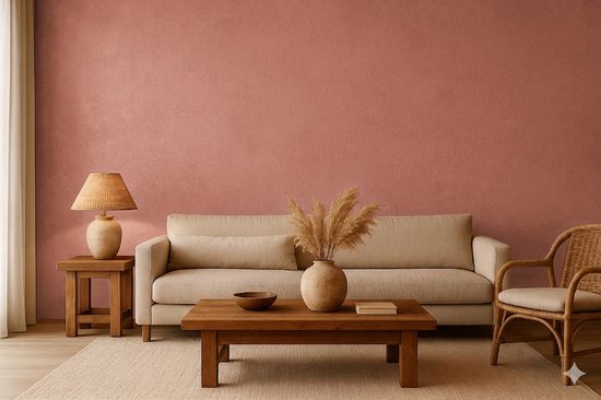 Een woonkamer met een roze muur, beige bank, rieten stoel, houten tafel en decoratie.